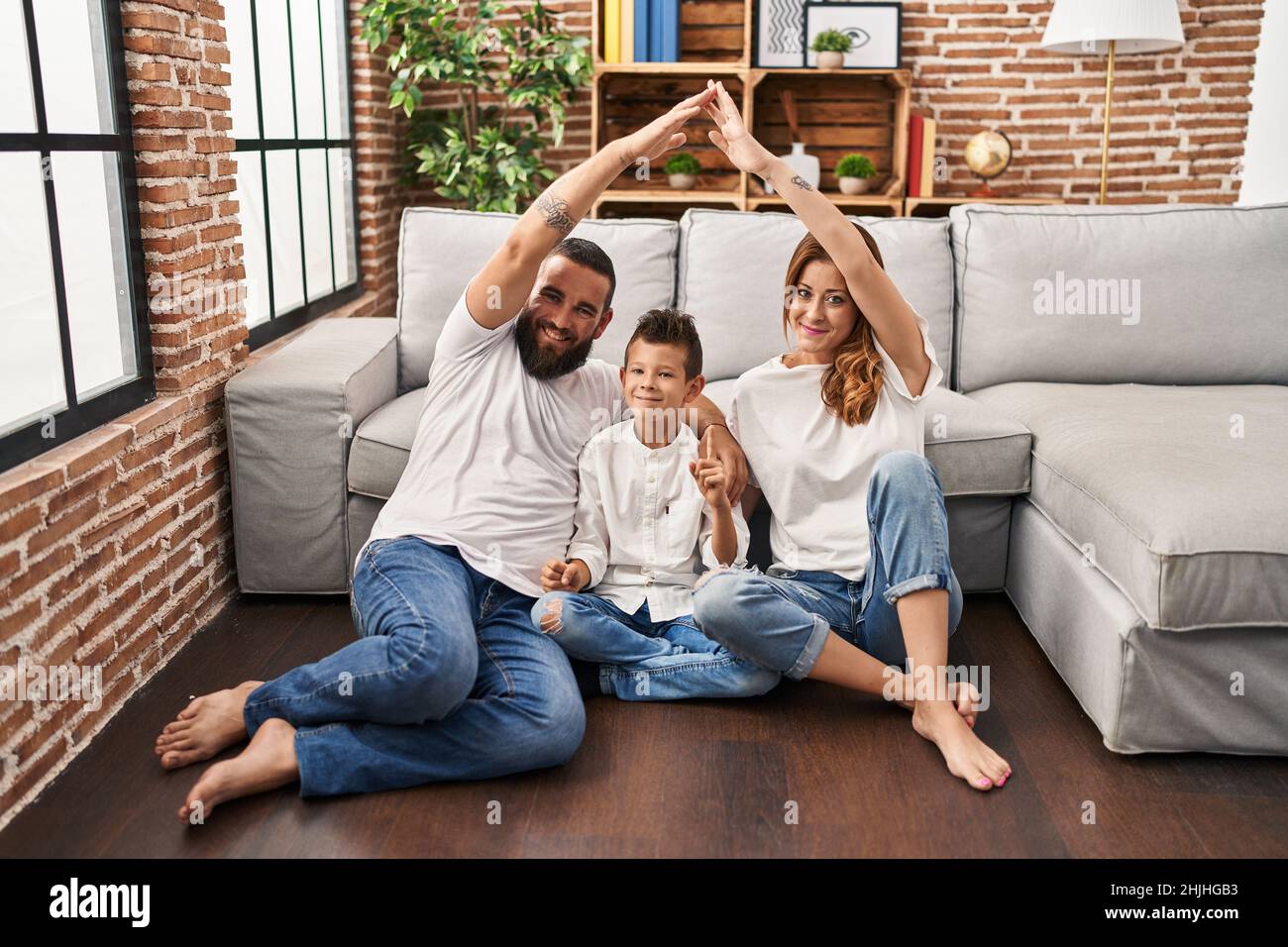 Family of three doing house shape with arms smiling with an idea or question pointing finger with happy face, number one Stock Photo
