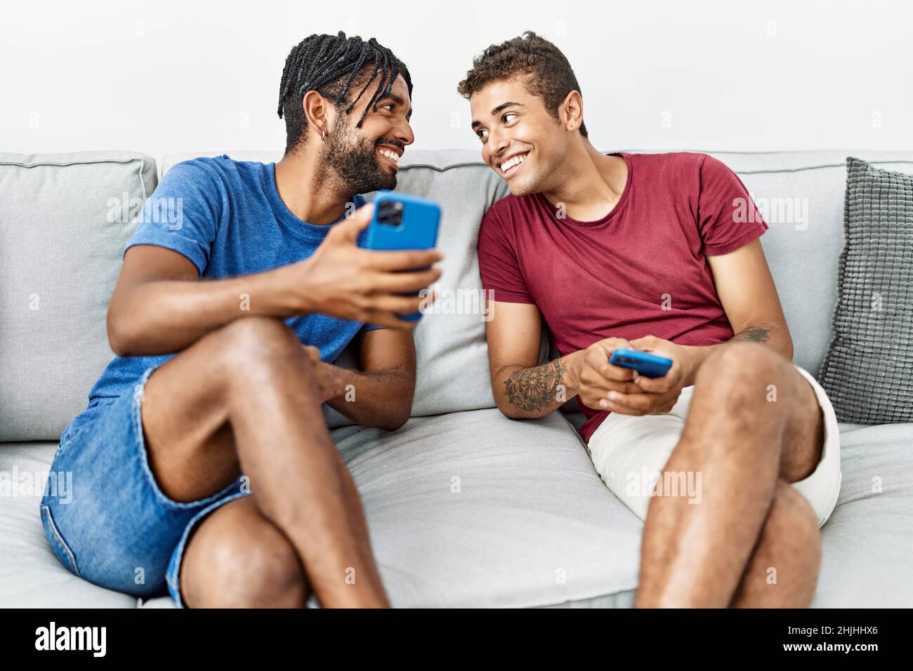 Two men friends using smartphone sitting on sofa at home Stock Photo
