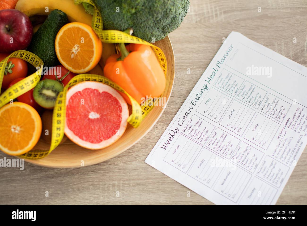Weekly eating meal planner and plate of fresh fruits and vegetables nearby on table Stock Photo