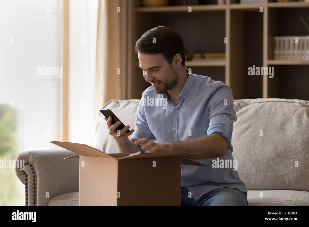 Happy young man leaving review in mobile shopping app. Stock Photo