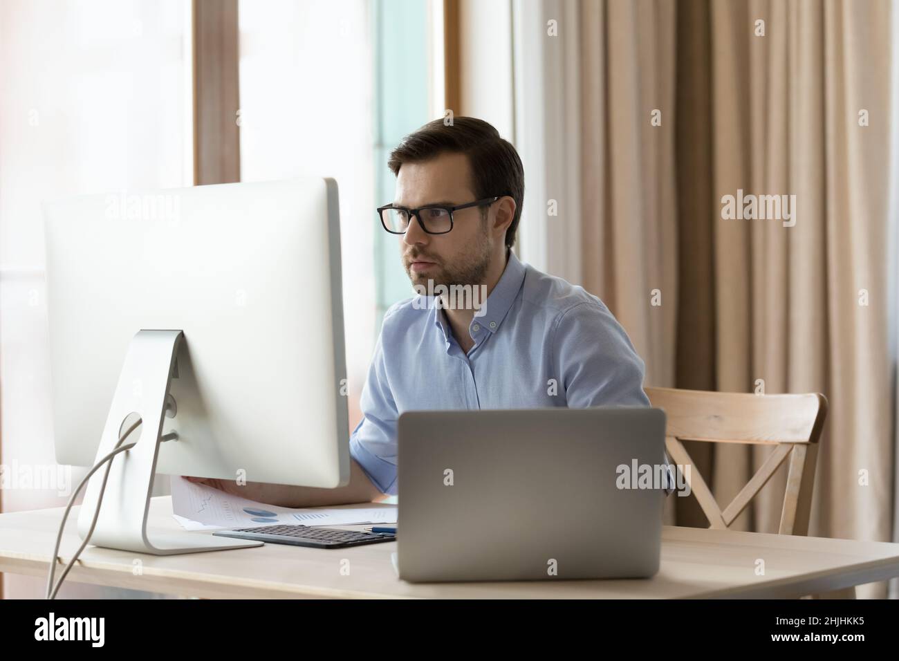 Concentrated young businessman in eyeglasses working on different devices. Stock Photo