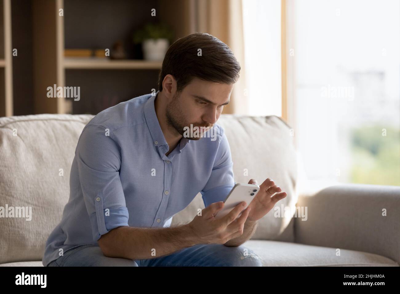 Concentrated young man using smartphone at home. Stock Photo