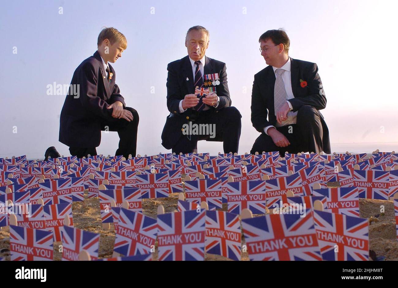2004: File photo dated June 2004 of WWII veteran Fred Matthews (centre), from Poole in Dorset, reading a message written by a Royal British Legion member on a Union Jack flag placed on the sands of Sword Beach in Hermanville, Normandy in northern France, as he is joined by his son Chris (right) and grandson Lee Edwards, 12. Issue date: Sunday January 30, 2022. Stock Photo