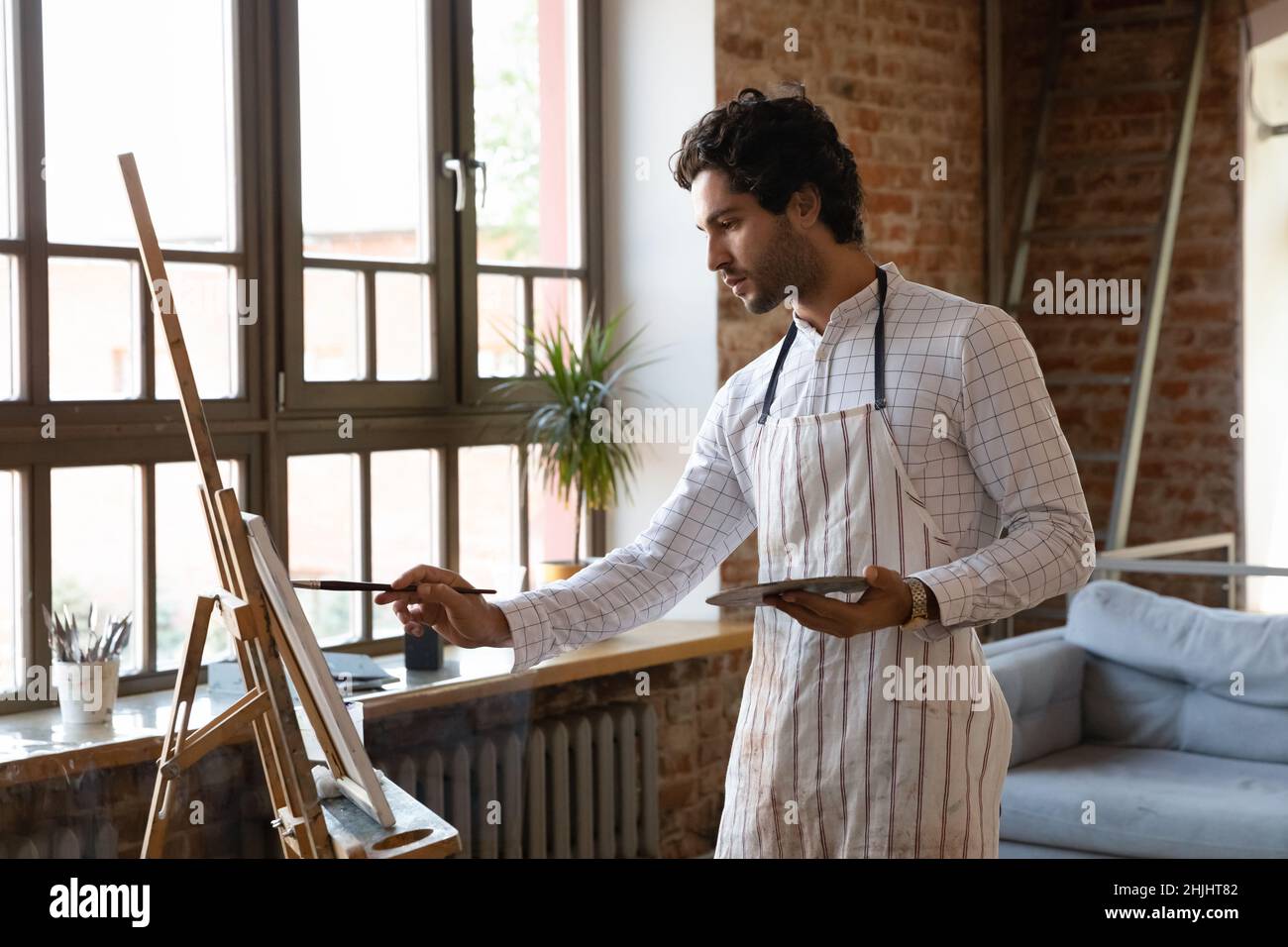 Thoughtful inspired young artist guy drawing at easel Stock Photo