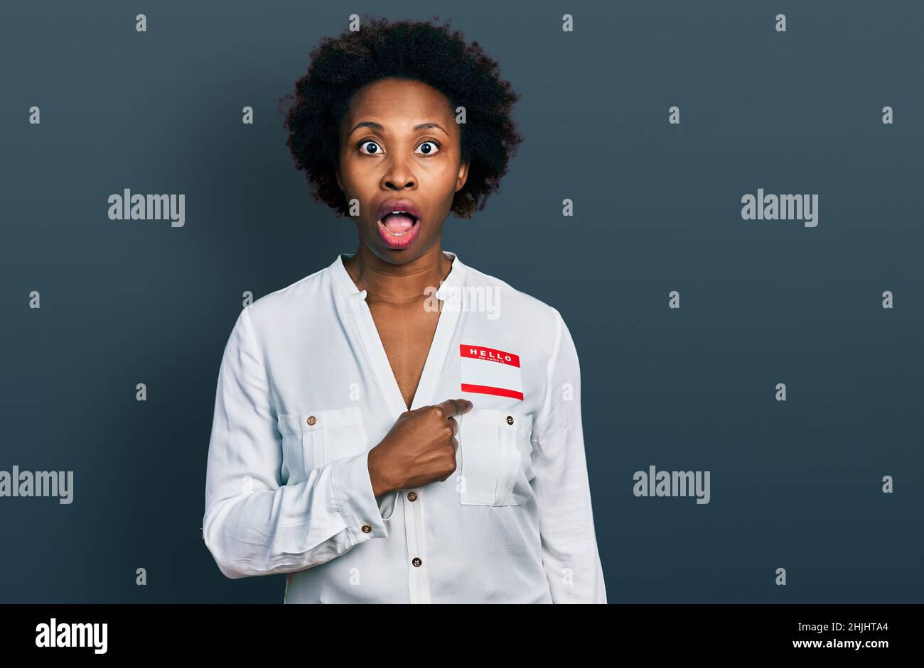 African american woman with afro hair wearing hello my name is sticker identification afraid and shocked with surprise and amazed expression, fear and Stock Photo