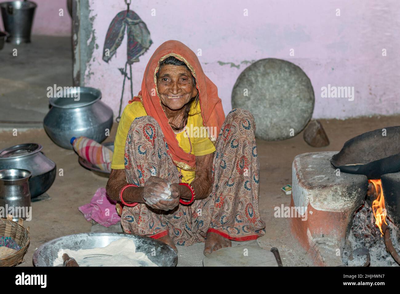 Grandmother making and cooking fresh food in a rural village in a vintage kitchen using firewood in earthen chulhas. smile on face. Stock Photo