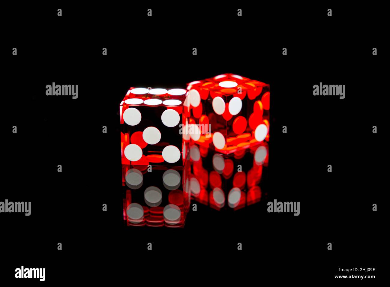 Professional casino-style dice on a reflective surface isolated against a black background. Stock Photo