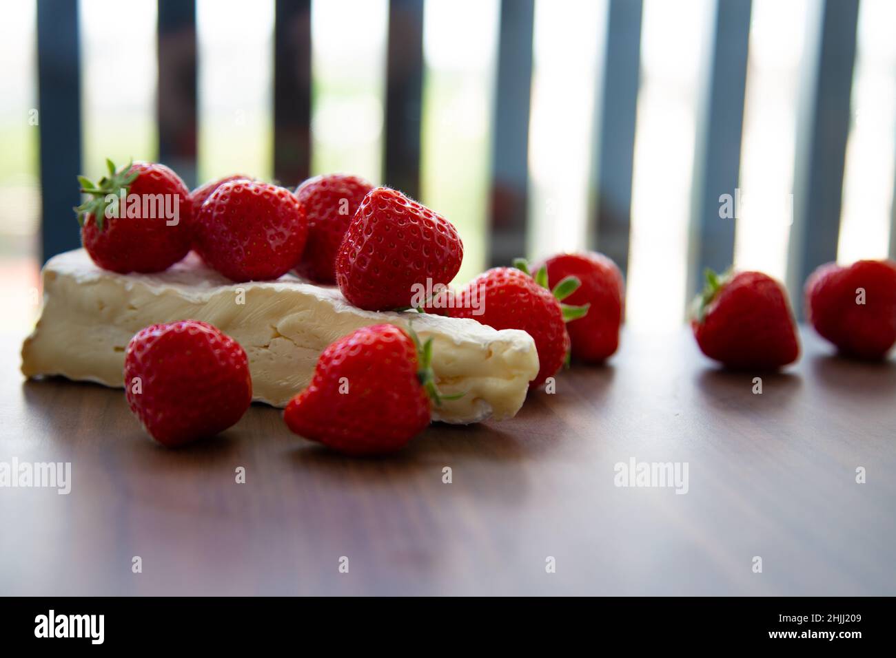 Strawberries accented on the pale backing of a wedghe of brie on a wooden board Stock Photo