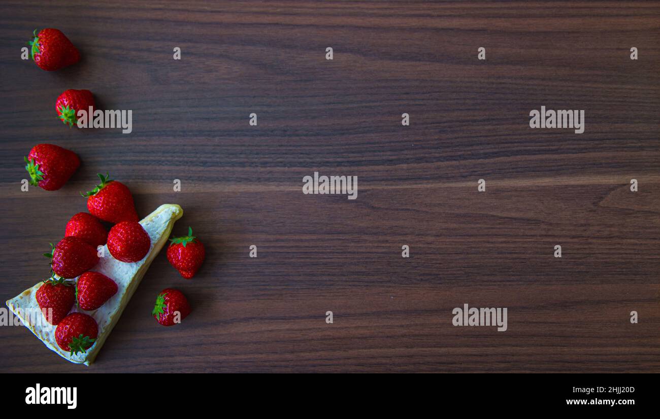 Strawberries accented on the pale backing of a wedghe of brie on a wooden board Stock Photo