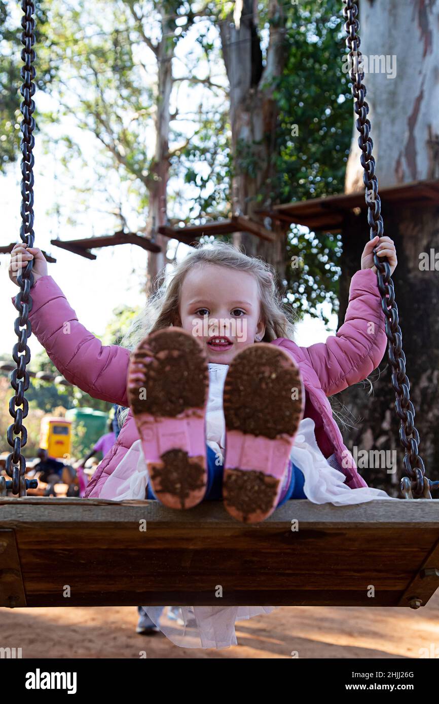 Young girl on a swing in a park with muddy wellington boots. Stock Photo