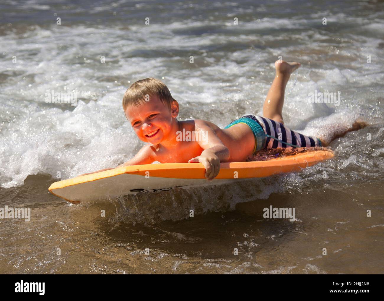 Young boy body boarding fearlessly in shallow waves. Stock Photo