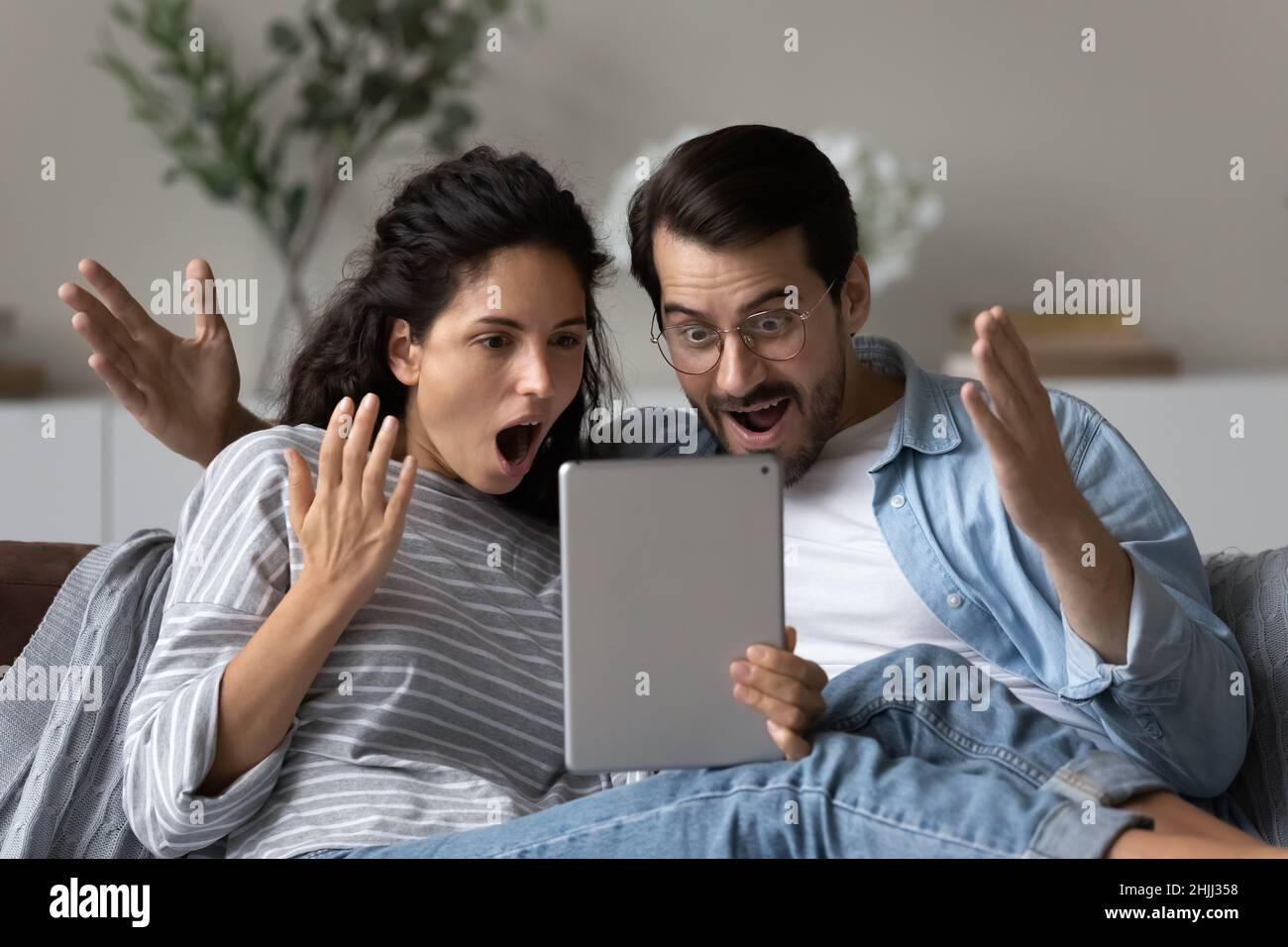 Astonished couple gawp at digital tablet feel amazed by news Stock Photo