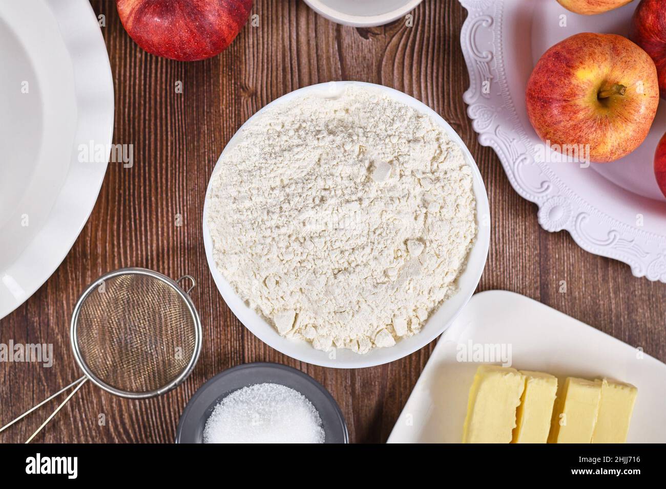Bowl of flour surrounded by other pie crust ingredients like butter and sugar on wooden background Stock Photo