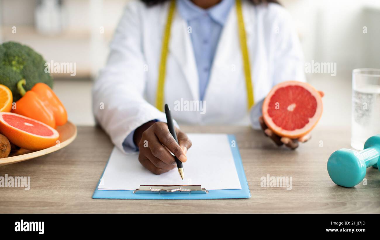 African american female dietologist holding grapefruit and writing