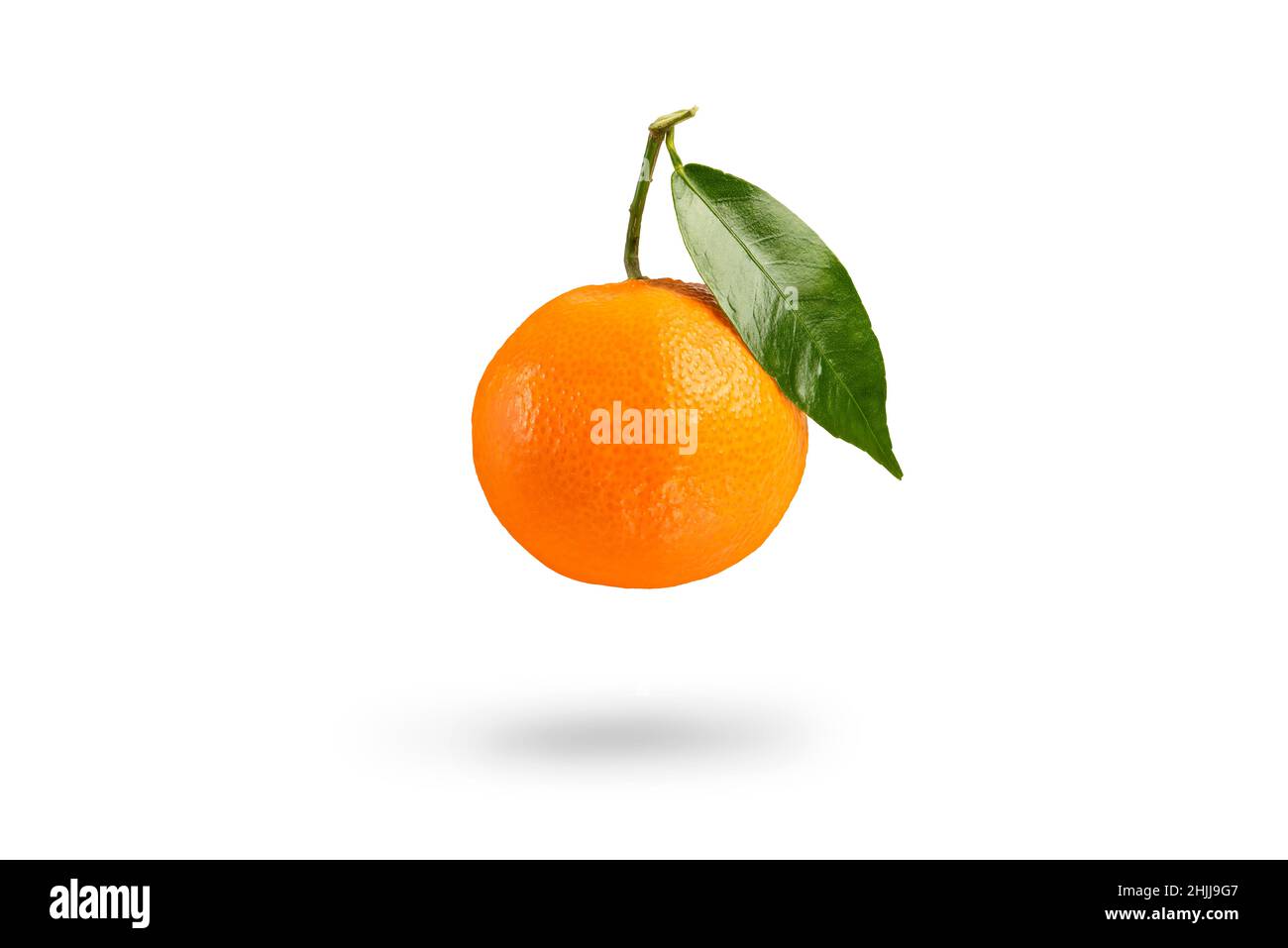 Tangerine with green leaf falls casting a shadow .Fresh tangerine on a white isolated background. Texture of mandarin close-up. Stock Photo