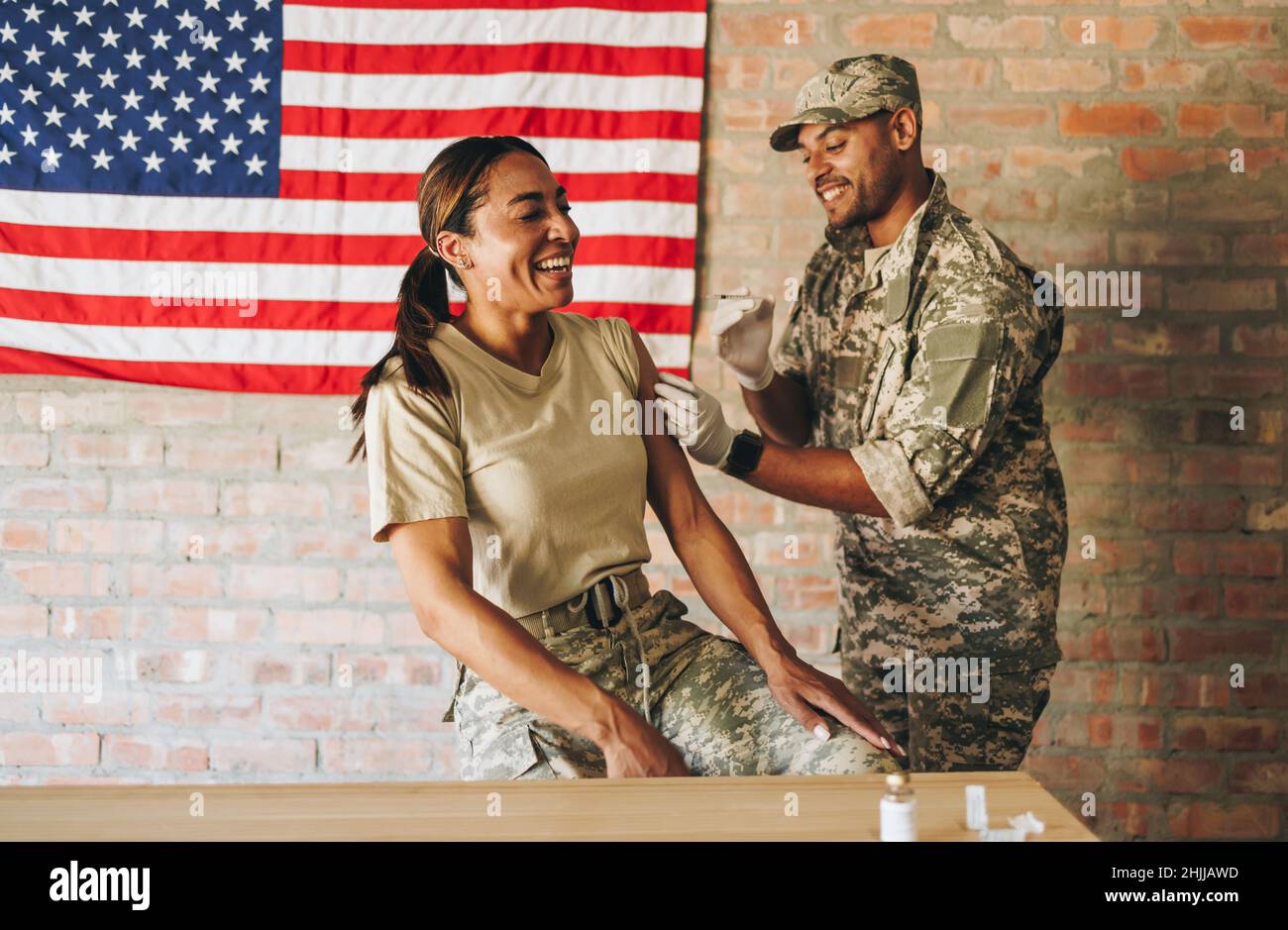 Cheerful servicewoman receiving a dose of the covid-19 vaccine in the military hospital. American female soldier laughing happily while getting inject Stock Photo