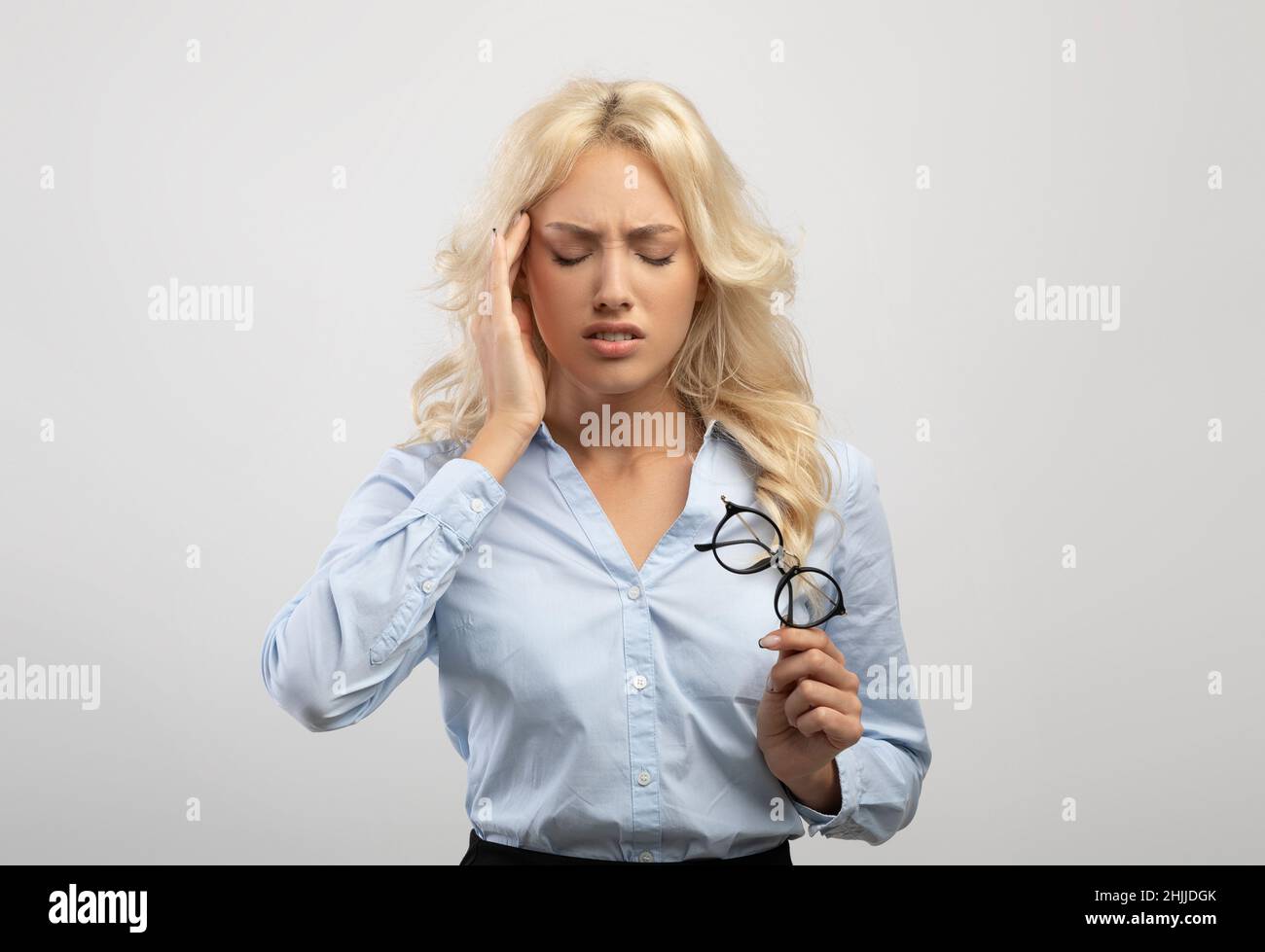 Overworked female office employee suffering from headache, standing on