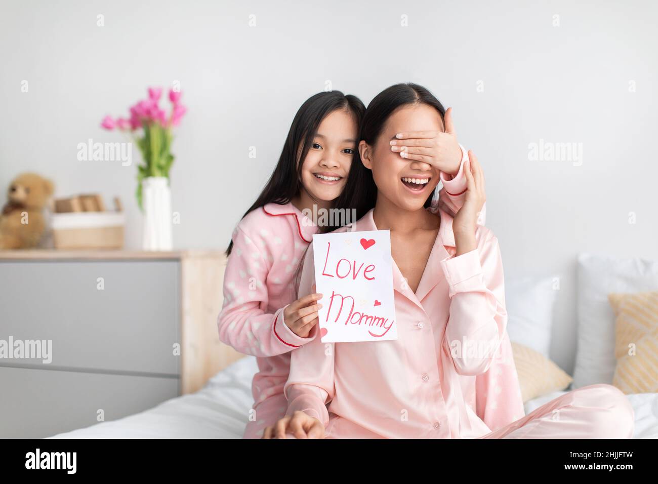 Satisfied chinese teenage girl closes eyes to young lady gives card and congratulates with mother day Stock Photo