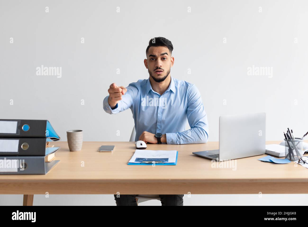 Arab man using laptop sitting at desk pointing at camera Stock Photo