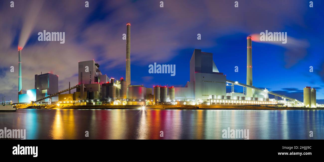 Large illuminated coal power plant with reflected lights in the water of a river Stock Photo