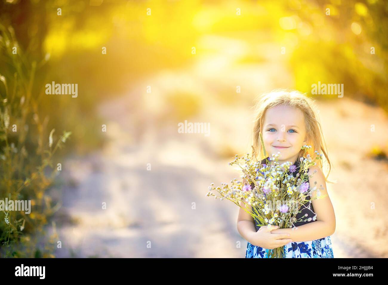 Cute little girl with a bouquet of wildflowers in the park at sunset ...