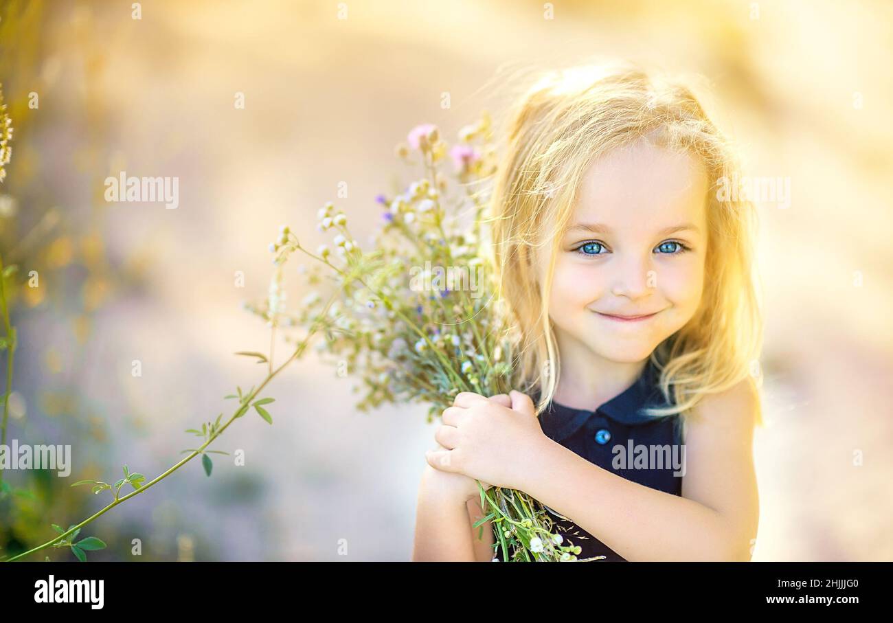 Cute little girl with a bouquet of wildflowers in the park at sunset ...