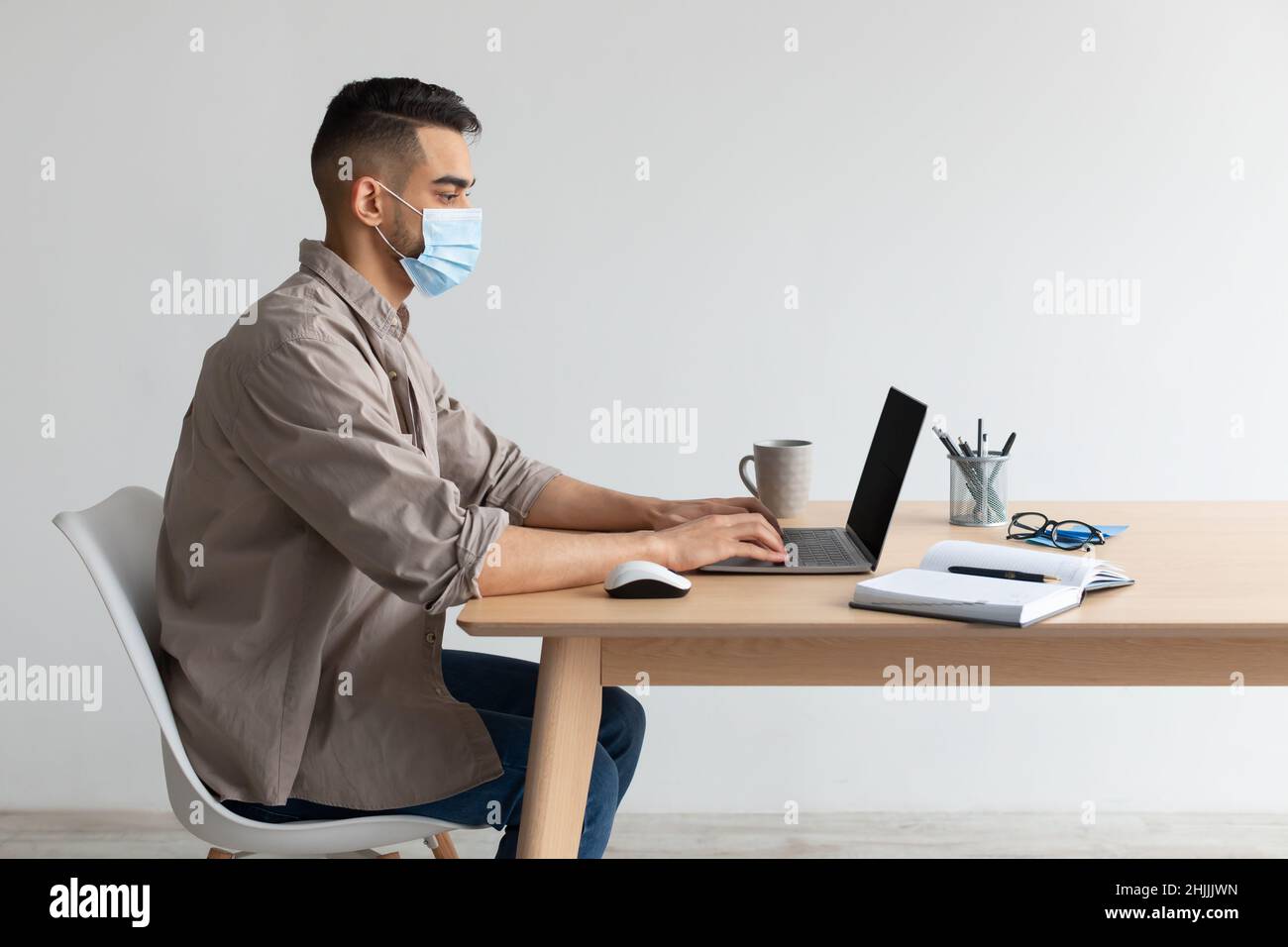 Man in protective facemask working on pc at home office Stock Photo