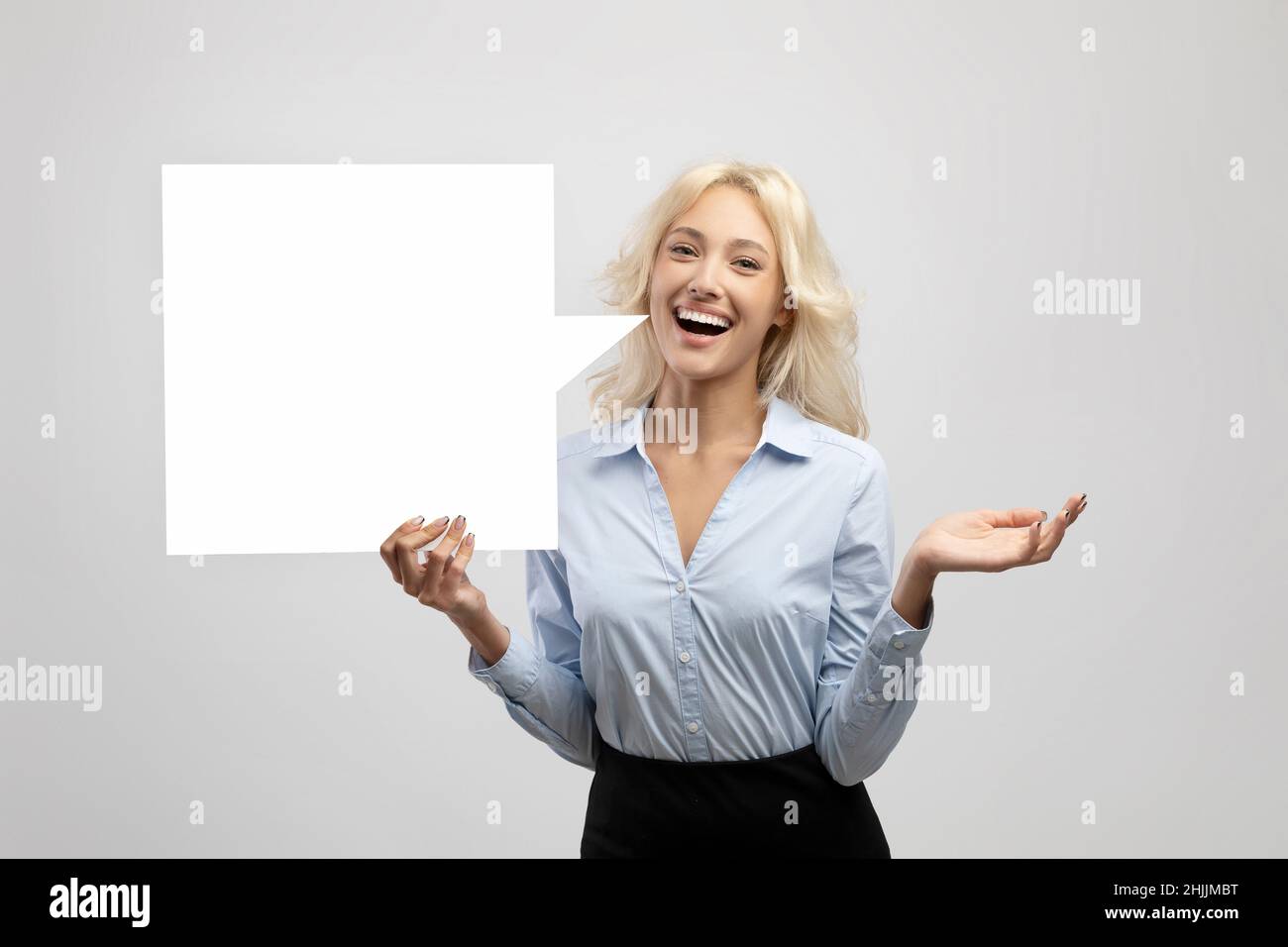Excited businesswoman holding empty speech bubble, standing over light grey studio background, space for design Stock Photo