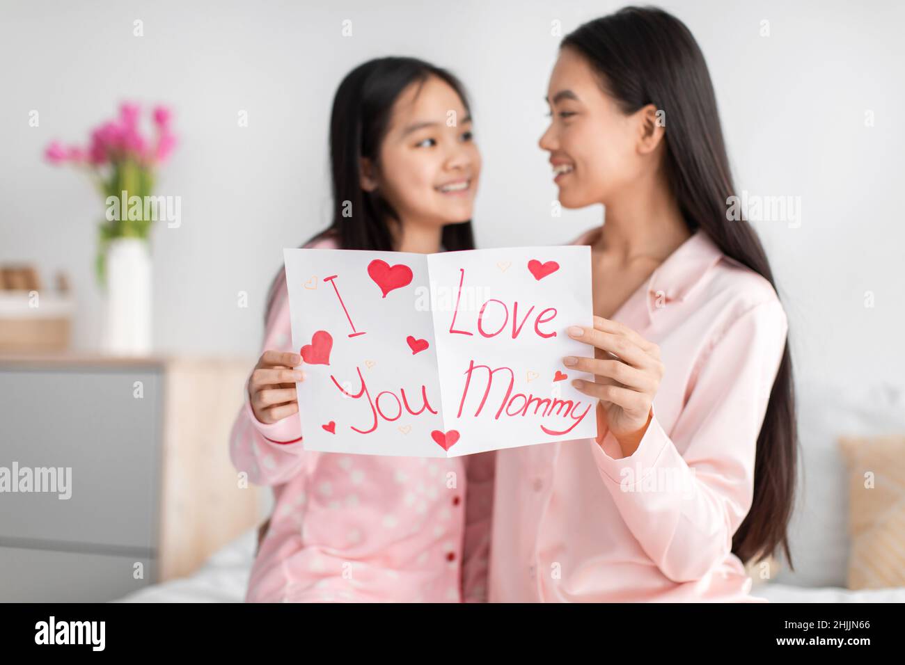 Satisfied happy korean young girl and millennial female read card and congratulate with mother day, sit on bed Stock Photo