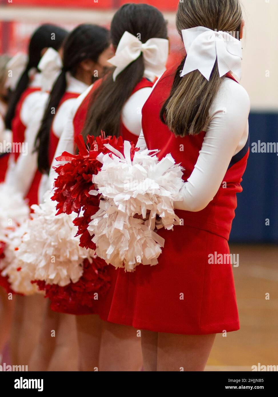 Cheerleaders standing with their pom poms behind them at a high school basketball game Stock Photo