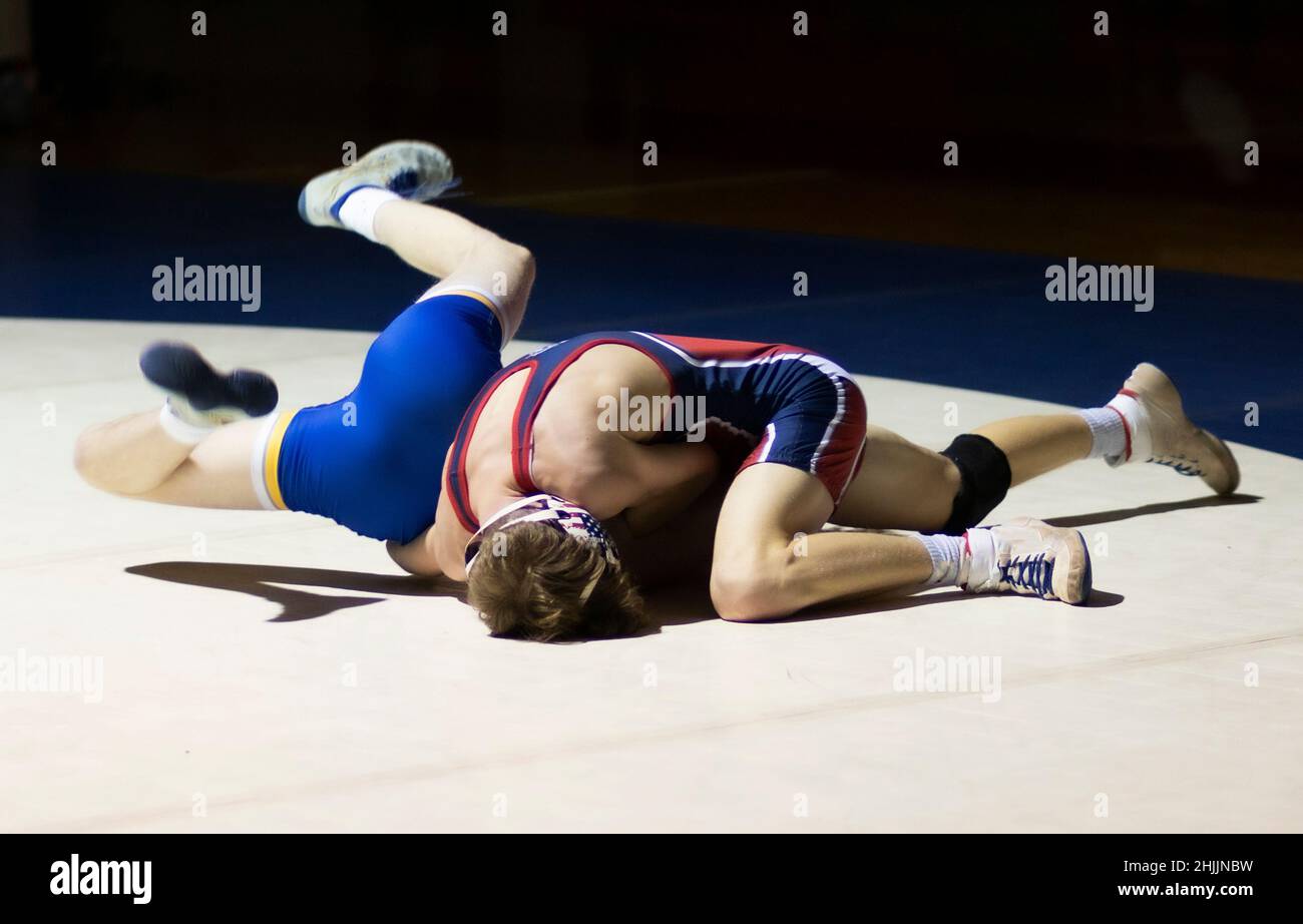Two high school wrestlers are wrestling under a spotlight in a gym