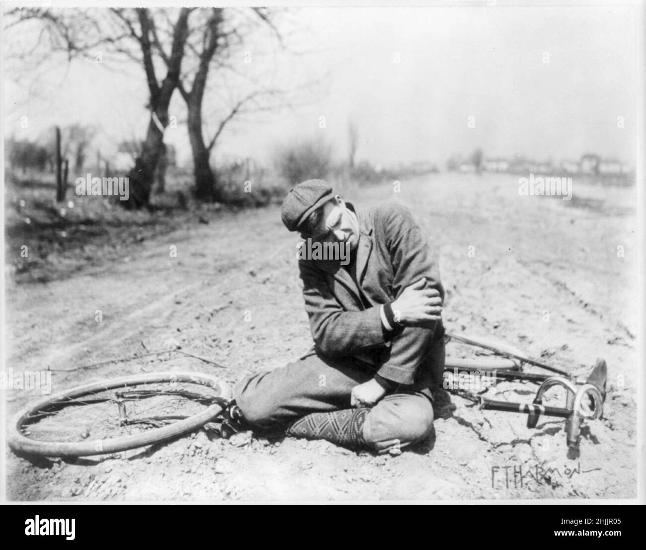 Man, with a broken bicycle, sitting in the dirt holding his arm - circa 1897 Stock Photo
