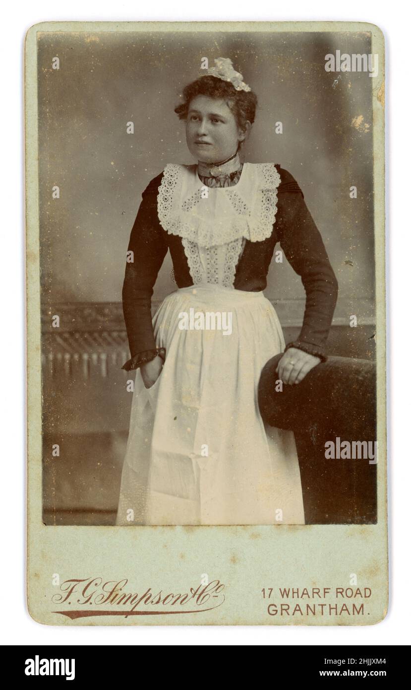 Original Victorian Carte de Visite (CDV) or visiting card of attractive maid, parlour maid, in uniform, wearing a white apron with bib and a lace cap, F.G. Simpson & Co. 17 Wharf Road, Grantham, Lincolnshire, U.K. circa 1888 Stock Photo