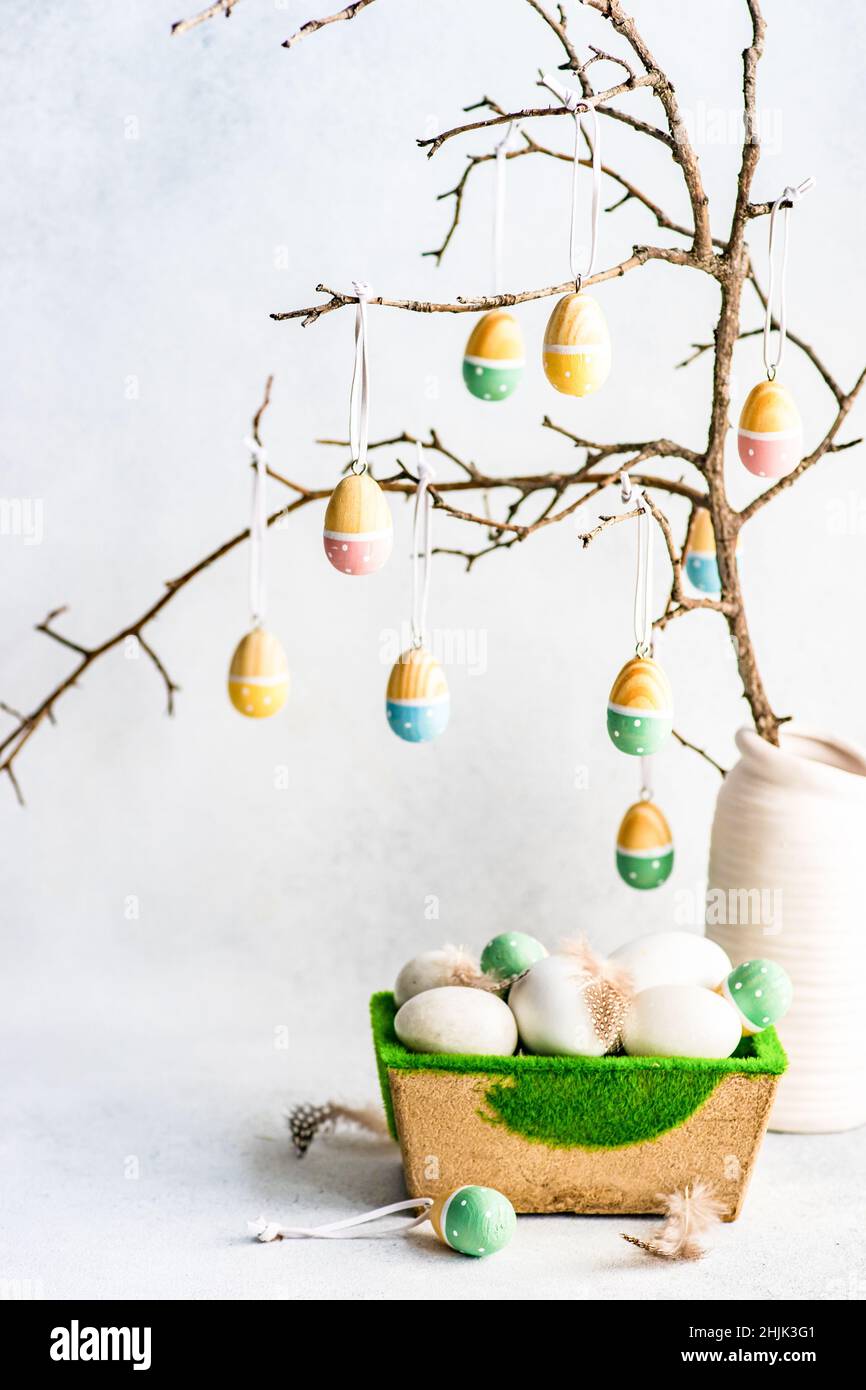 Painted Easter egg decorations hanging on branches next to a box of Easter eggs Stock Photo