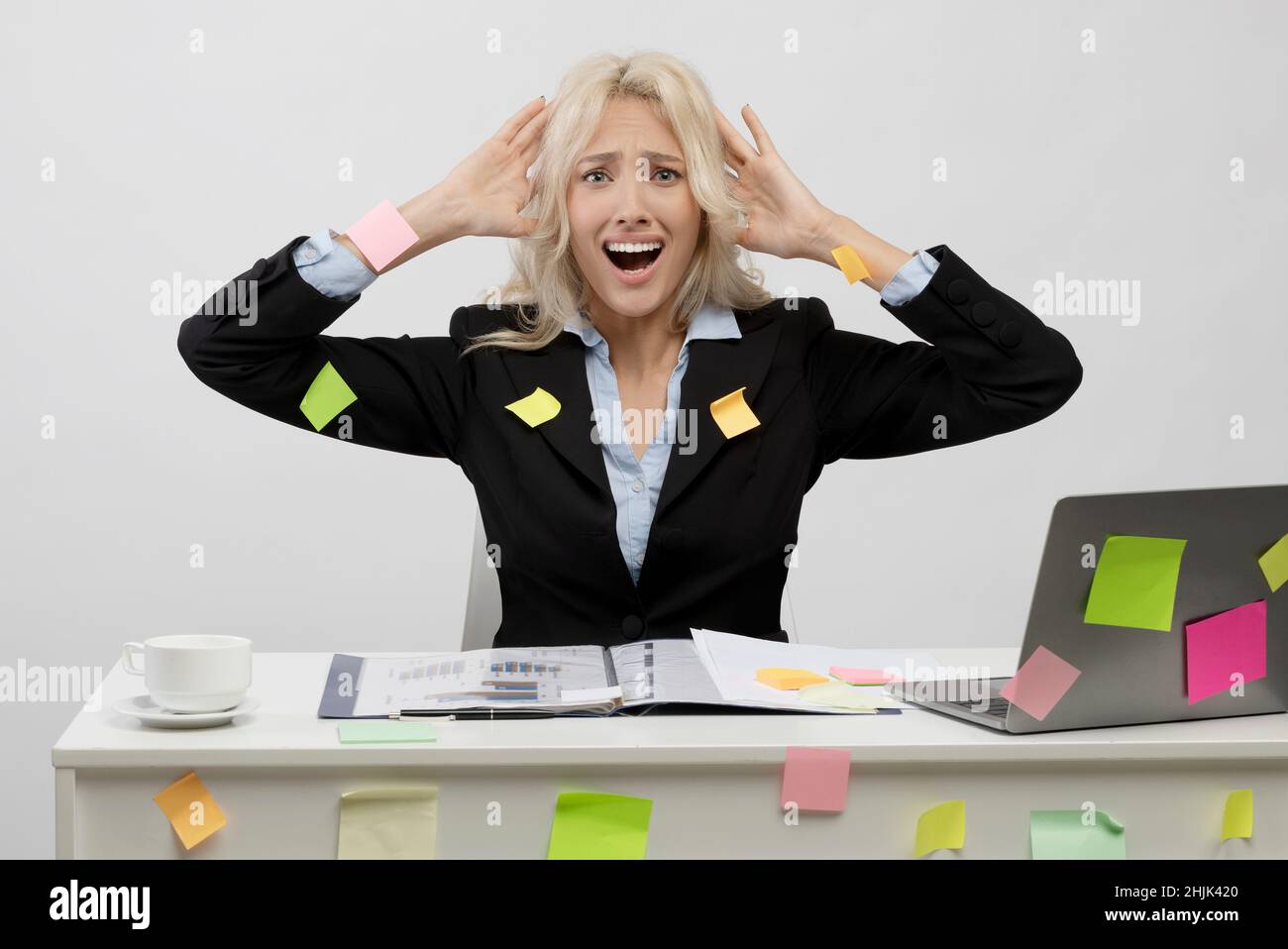 Shocked businesswoman covered in sticky papers, amazed got trouble deadline, sitting at workplace with laptop Stock Photo