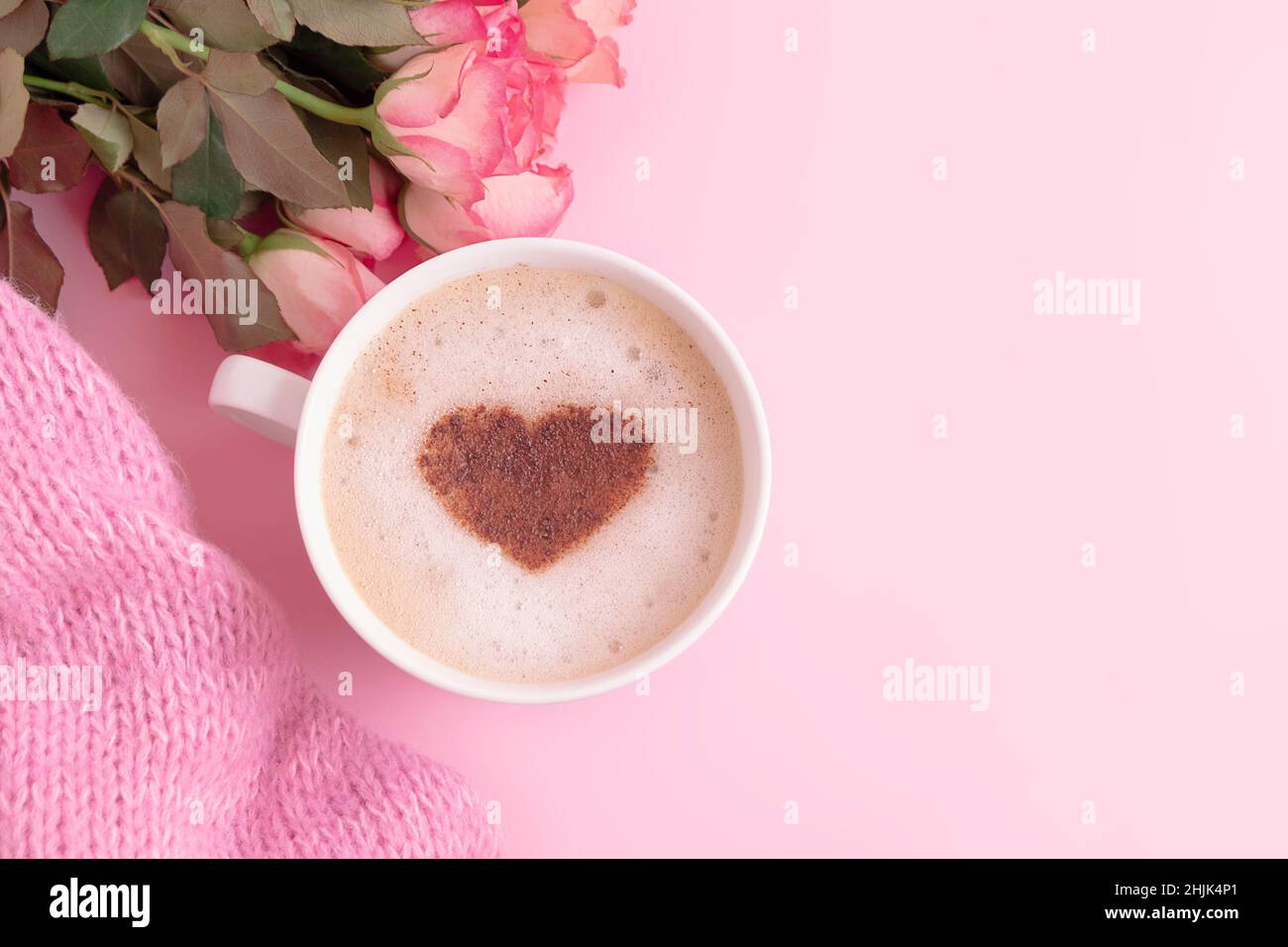 Romantic composition with coffee cup with heart on top, flowers and knitted blanket on pastel pink background and copy space Stock Photo