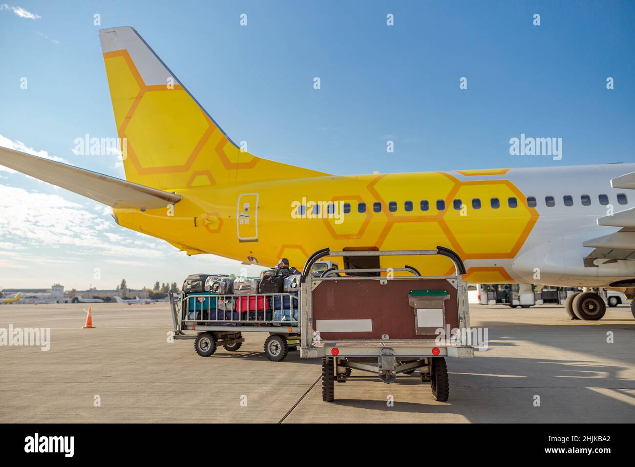 Yellow passenger airplane and baggage cart with travel bags under blue