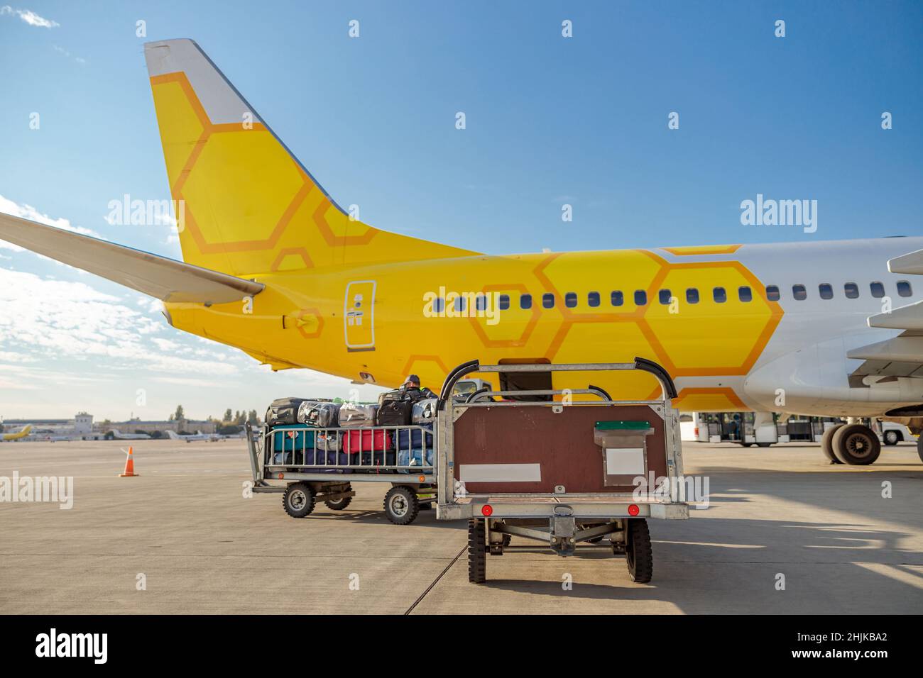 Yellow passenger airplane and baggage cart with travel bags under blue sky at airport Stock Photo