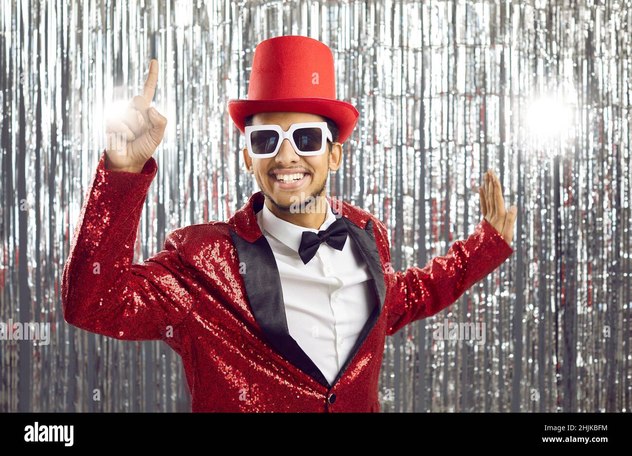 Happy young man in a shiny party jacket and tophat has an idea and points his finger up Stock Photo