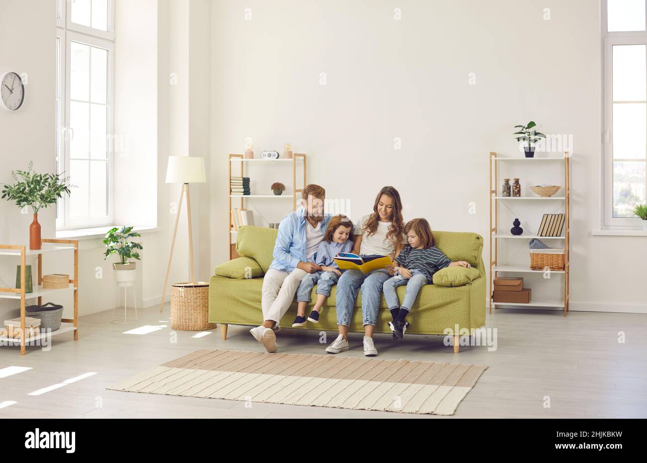 Happy family reading a book while sitting together on a couch in a modern living room Stock Photo