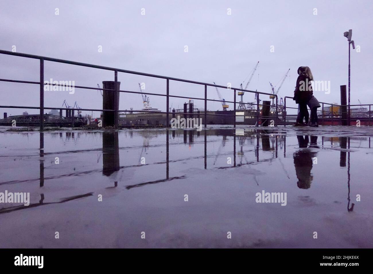 Hamburg, Germany. 30th Jan, 2022. Passers-by stand on a quay wall at the fish market in Hamburg harbor, where large puddles of water have formed after the storm surge. Earlier, storm depression 'Nadia' had swept across northern Germany with dangerous gusts. A severe storm surge submerged the fish market in Hamburg's Altona district. Credit: Marcus Brandt/dpa/Alamy Live News Stock Photo