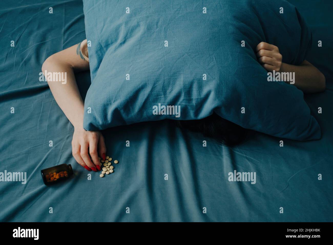 A young woman lies on the bed with her head under the pillow Stock