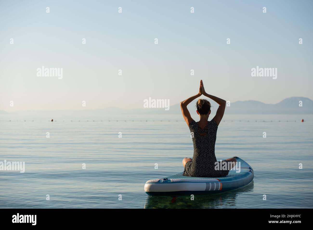 View from behind of a mindful young woman sitting in lotus position ...