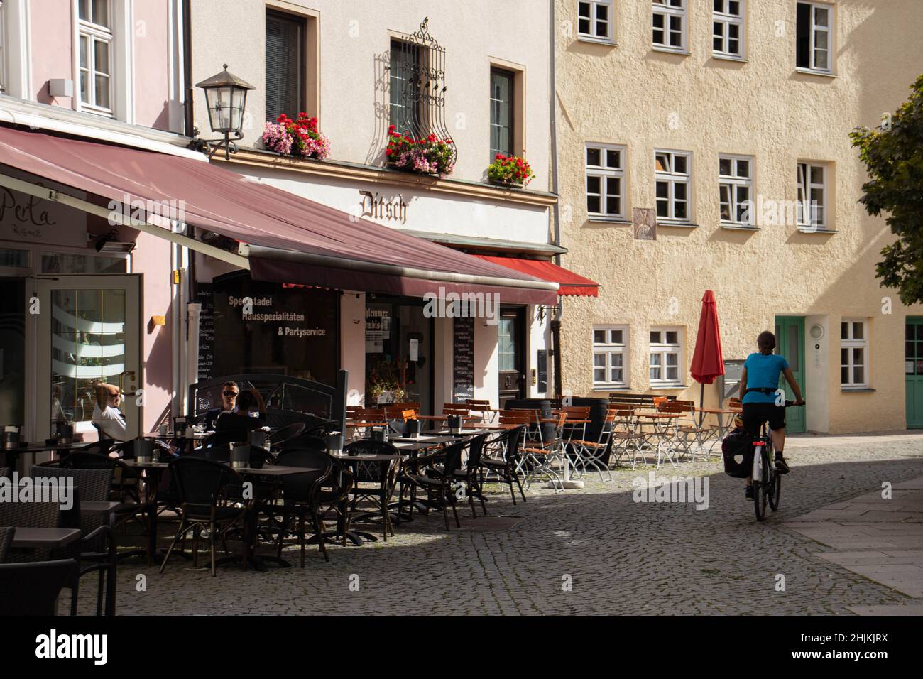 Eien Radfahrerin fährt an Restaurants vorbei. Die Fußgängerzone hat Kopfsteinpflaster. Stock Photo