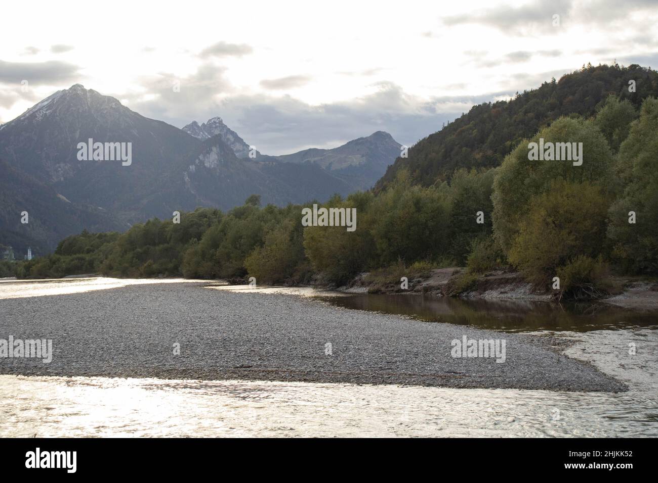 Blick vom Ufer des Lechs auf den Fluss Lech im abendlichen Gegenlicht mit Bergen im Hintergrund Stock Photo