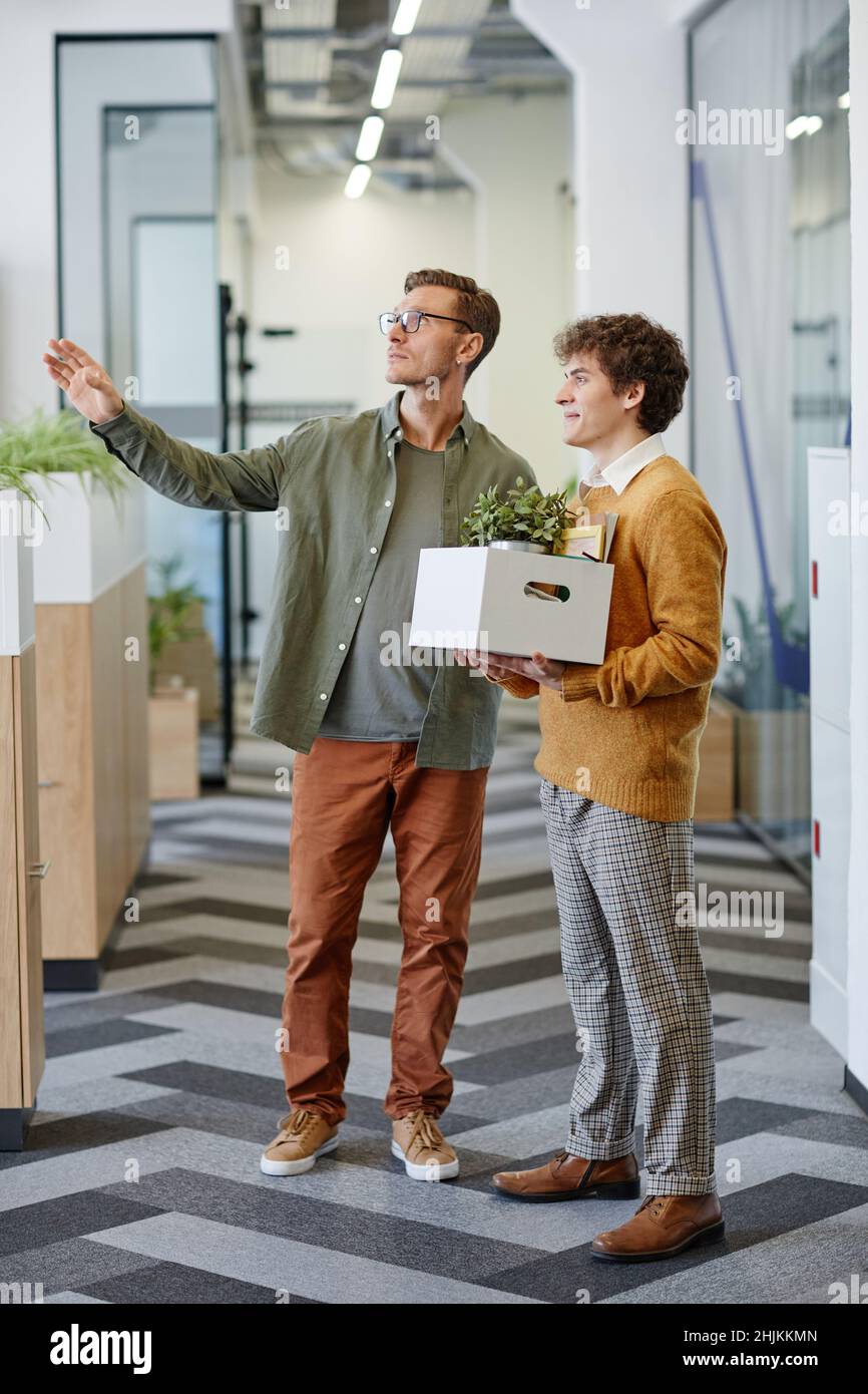 Full length portrait of smiling male manager welcoming new employee in office and showing workplace Stock Photo
