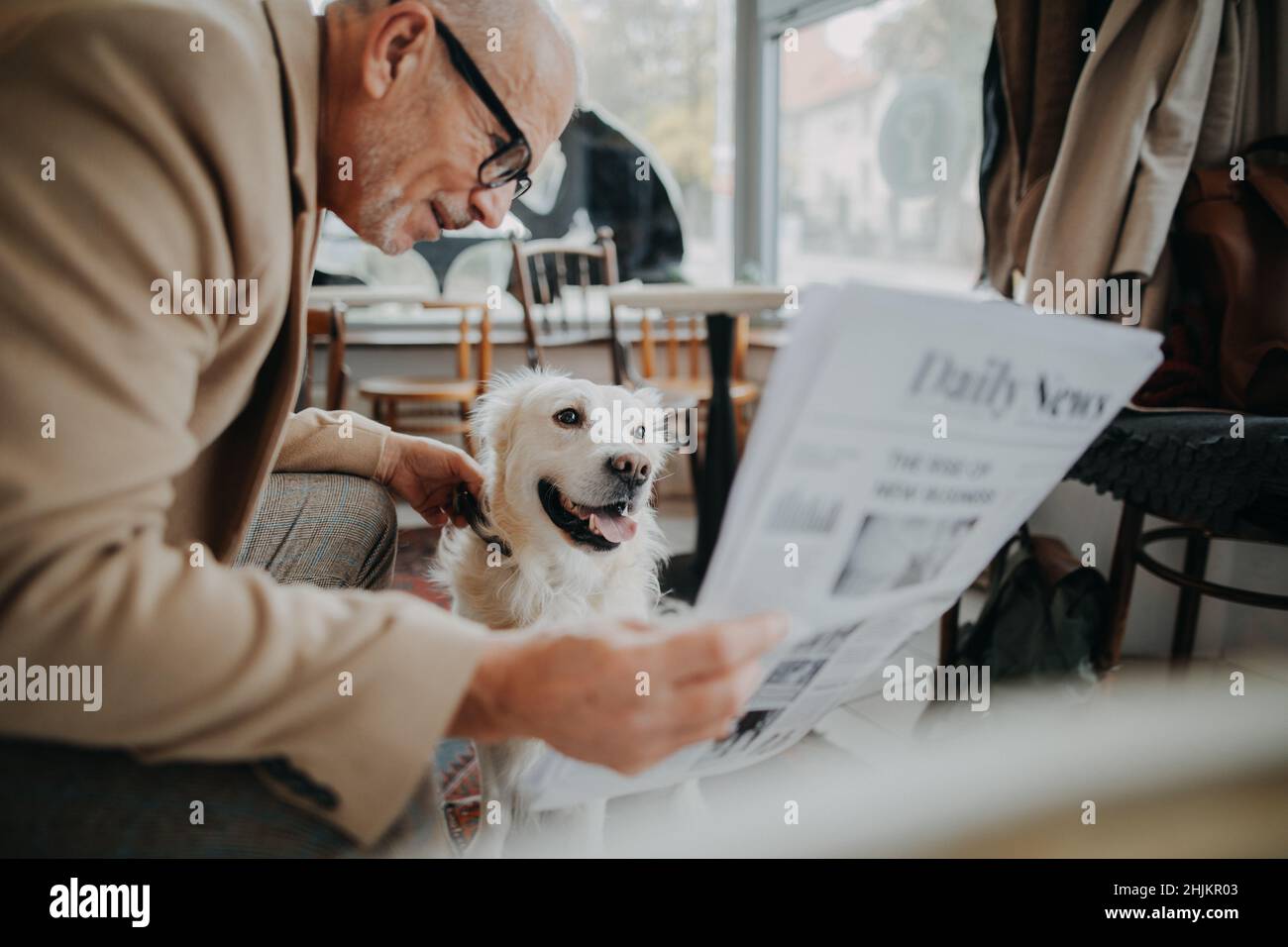 Happy senior man sitting in cafeteria and reading newspaper with his dog. Stock Photo