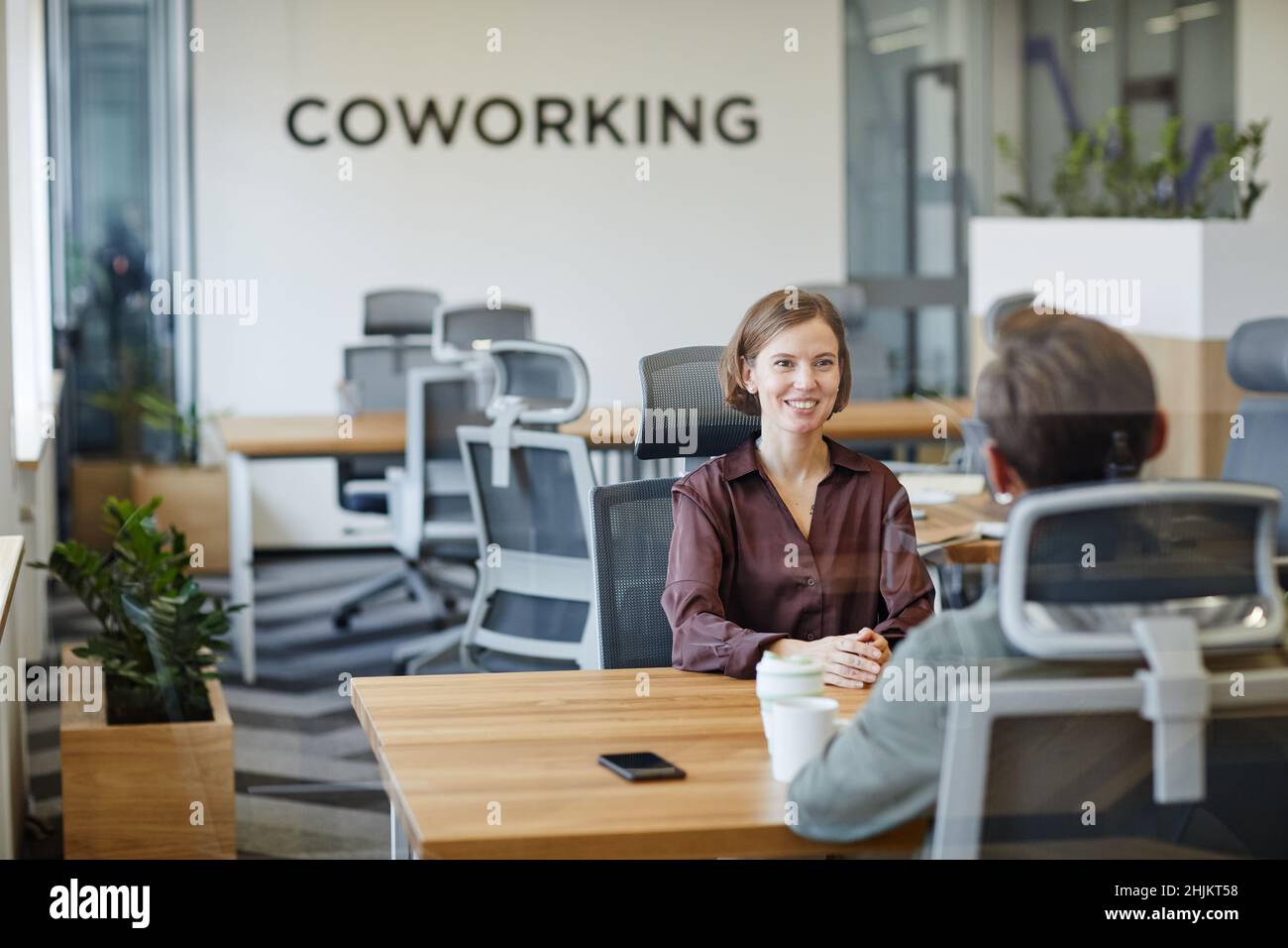Portrait of smiling young woman in job interview at office behind glass ...