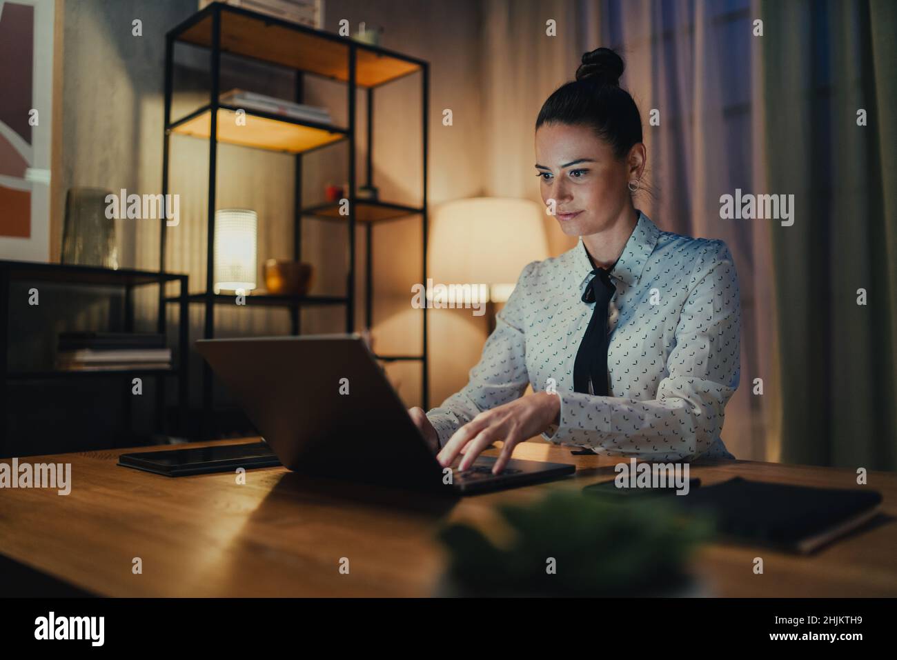 Happy mid adult business woman working on laptop in office at night. Stock Photo