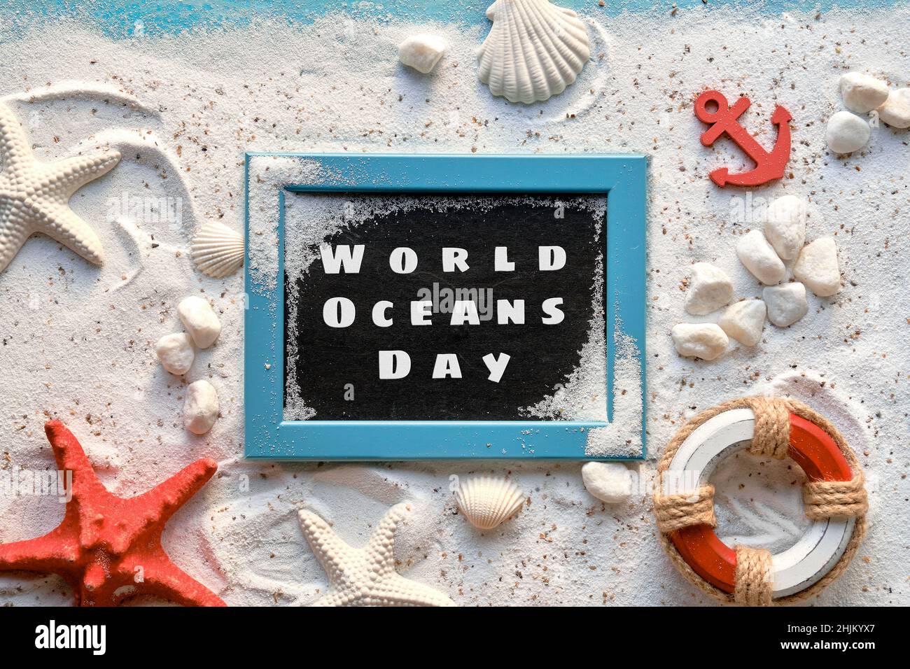 World Oceans Day text. Background with white sand on turquoise blue. Shells, red starfish, anchor. Stock Photo